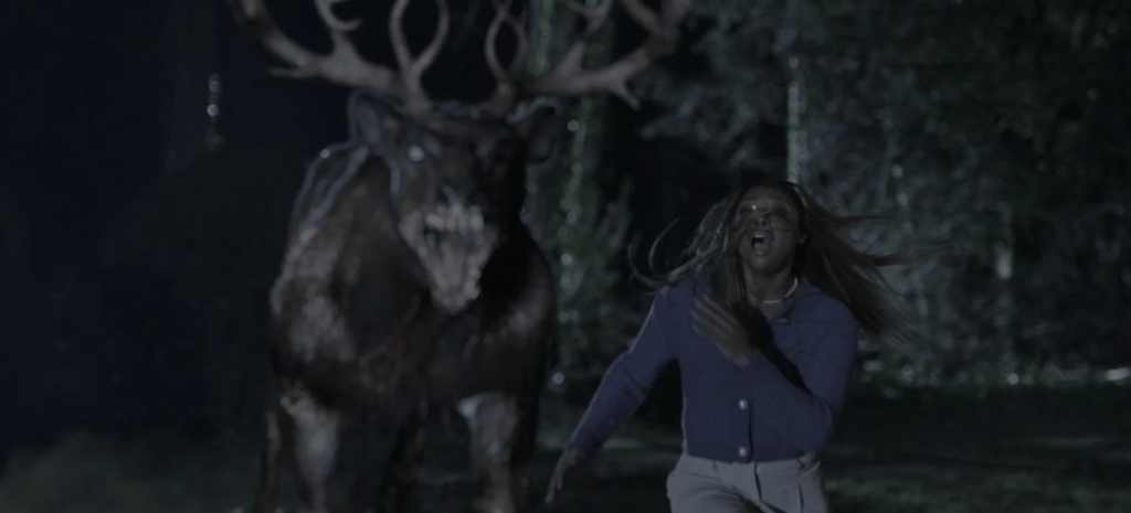 Eine Frau rennt in Panik durch einen dunklen Wald, während hinter ihr ein monströses, hirschähnliches Wesen mit gewaltigem Geweih und fletschenden Zähnen auf sie zurast – eine intensive Verfolgungsszene aus Bambi: The Reckoning (2025).