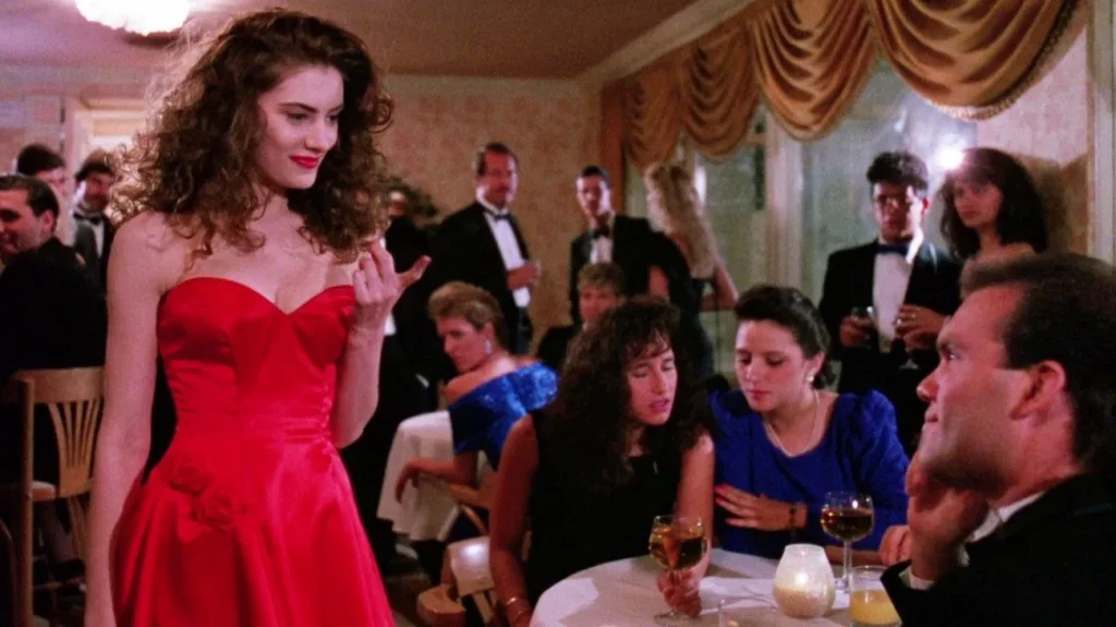 Eine Frau in einem leuchtend roten Kleid steht selbstbewusst in einem eleganten Restaurant und zeigt einem Mann am Tisch den Mittelfinger – Szene aus I’m Dangerous Tonight (1990).