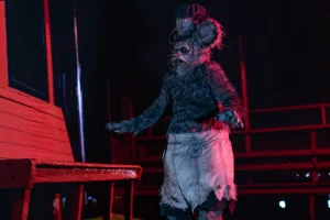 Figur im Rattenkostüm aus dem Film Screamboat steht auf einer rot beleuchteten Bühne